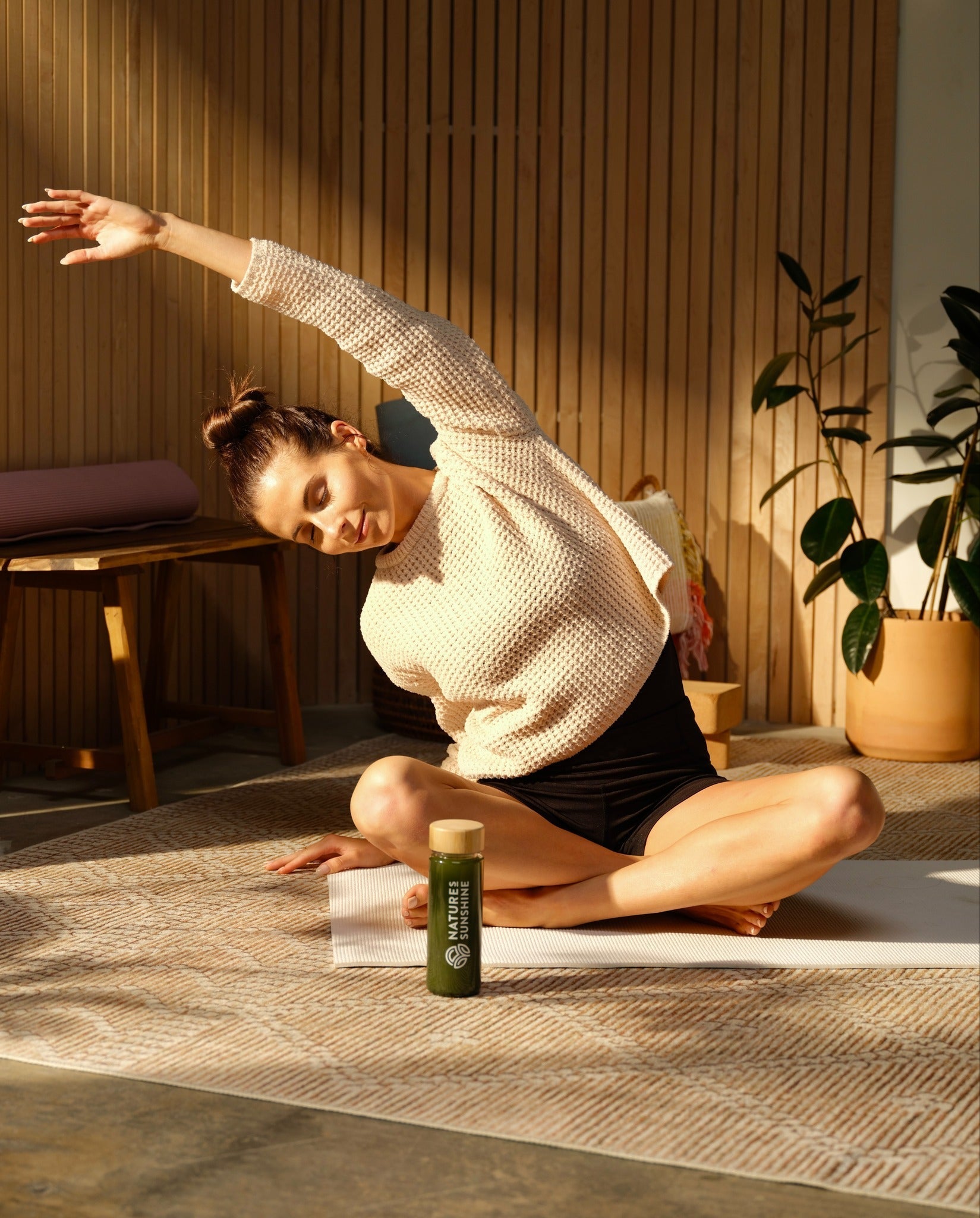 Woman on floor doing stretches with Nature Sunshine drink bottle