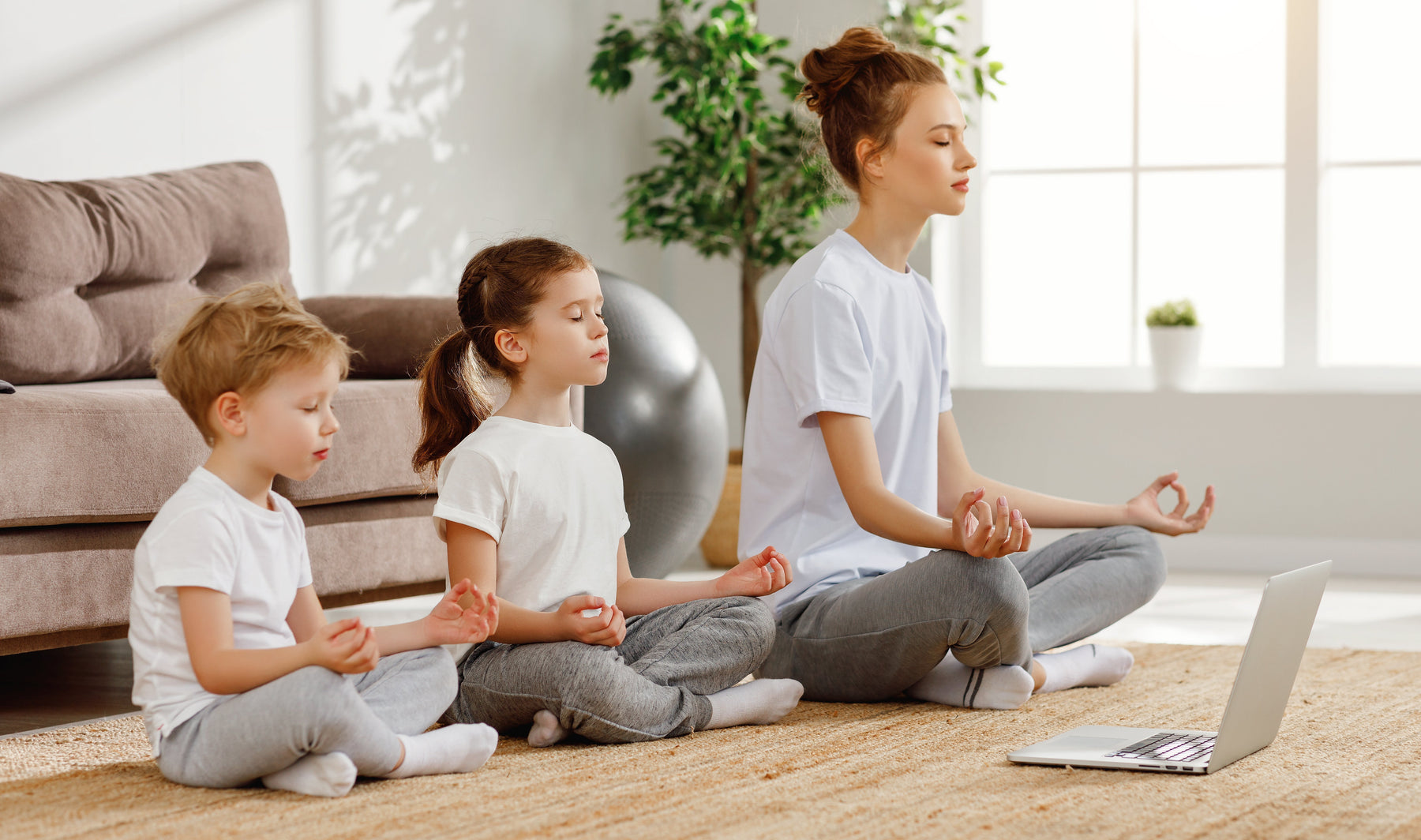 Mother with young son and daughter sitting on carpet in lounge in calm yoga pose