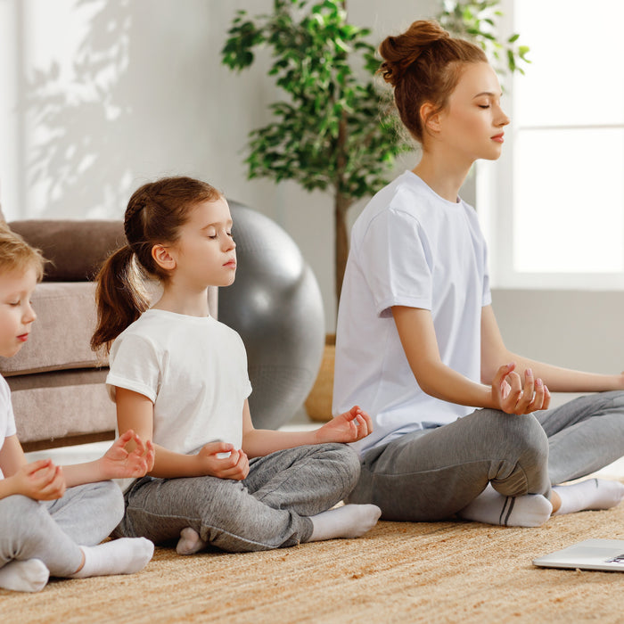Mother with young son and daughter sitting on carpet in lounge in calm yoga pose
