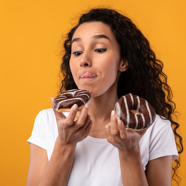 woman holding 2 chocolate donuts licking lips