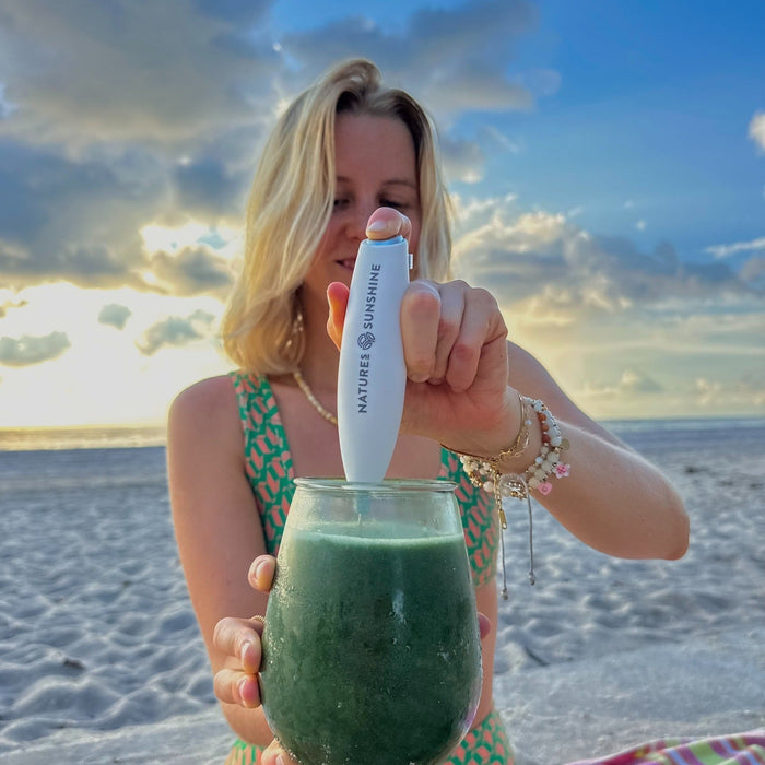 woman in swimsuit on beach mixing natures sunshine chlorophyll drink