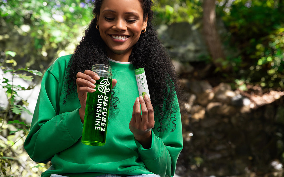 women in nature holding natures sunshine drink bottle and chlorophyll stick pack