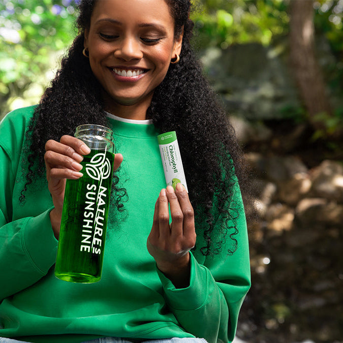 women in nature holding natures sunshine drink bottle and chlorophyll stick pack